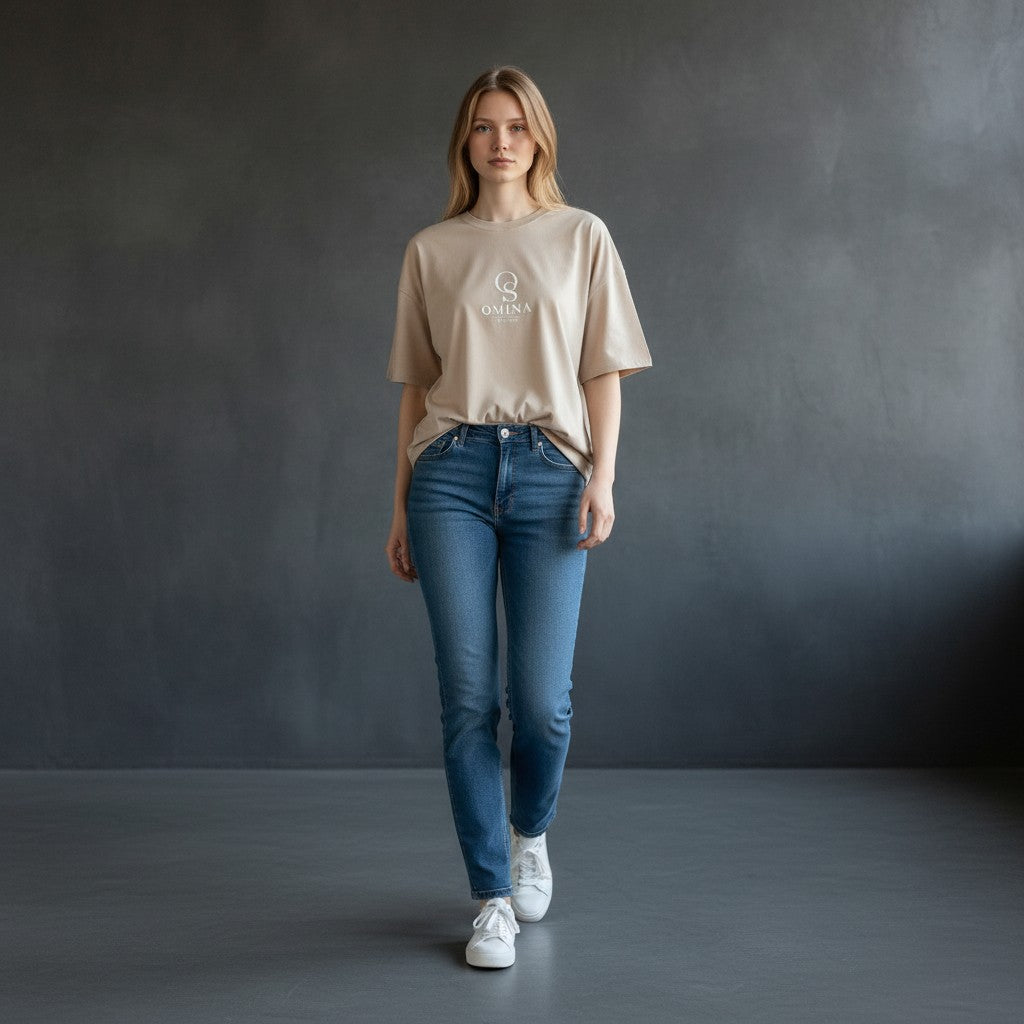 Omina beige heavyweight cotton boxy t-shirt with raw edge detail and subtle logo, worn by a woman with hands in pockets.