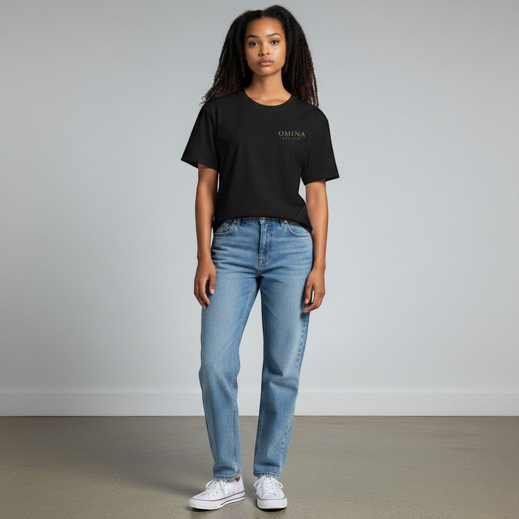 Omina Studio black cotton t-shirt with minimalist gold logo on chest, worn by a woman with light wash jeans.