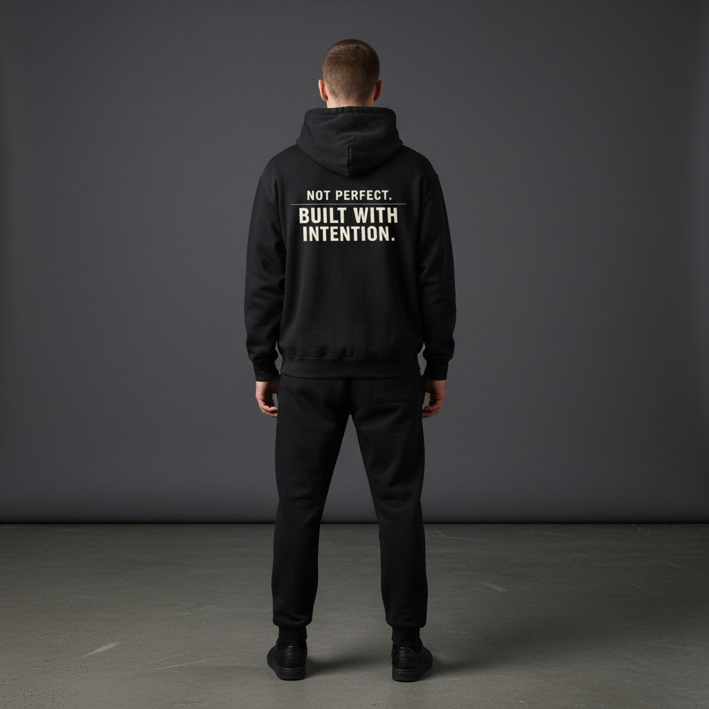 Omina black fleeced boxy hoodie with "NOT PERFECT. BUILT WITH INTENTION." graphic on back.