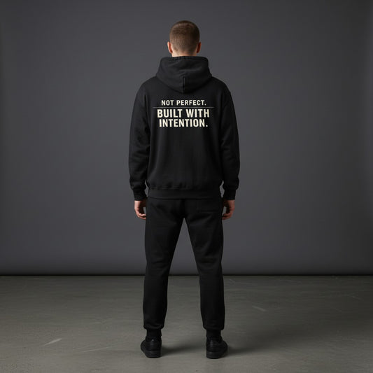Omina black fleeced boxy hoodie with "NOT PERFECT. BUILT WITH INTENTION." graphic on back.