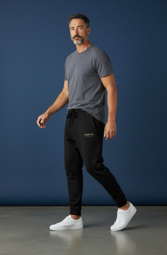 Omina Studio black heavyweight cotton-blend fleece sweatpants with a relaxed fit and subtle gold logo detail on the left thigh.