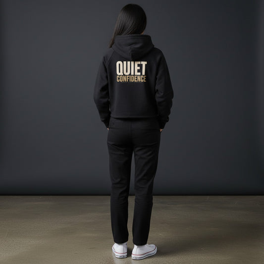 Omina black cropped zip-through hoodie with "QUIET CONFIDENCE" graphic on back. Soft premium fabric, relaxed fit, adjustable hood.
