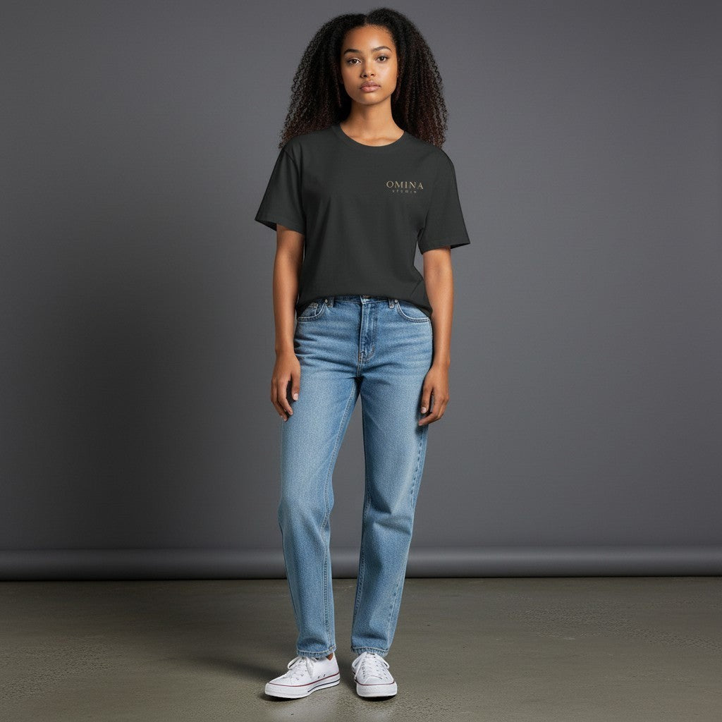 Omina Studio dark grey premium cotton t-shirt with minimal gold typography on the chest, worn by a woman with light wash jeans.