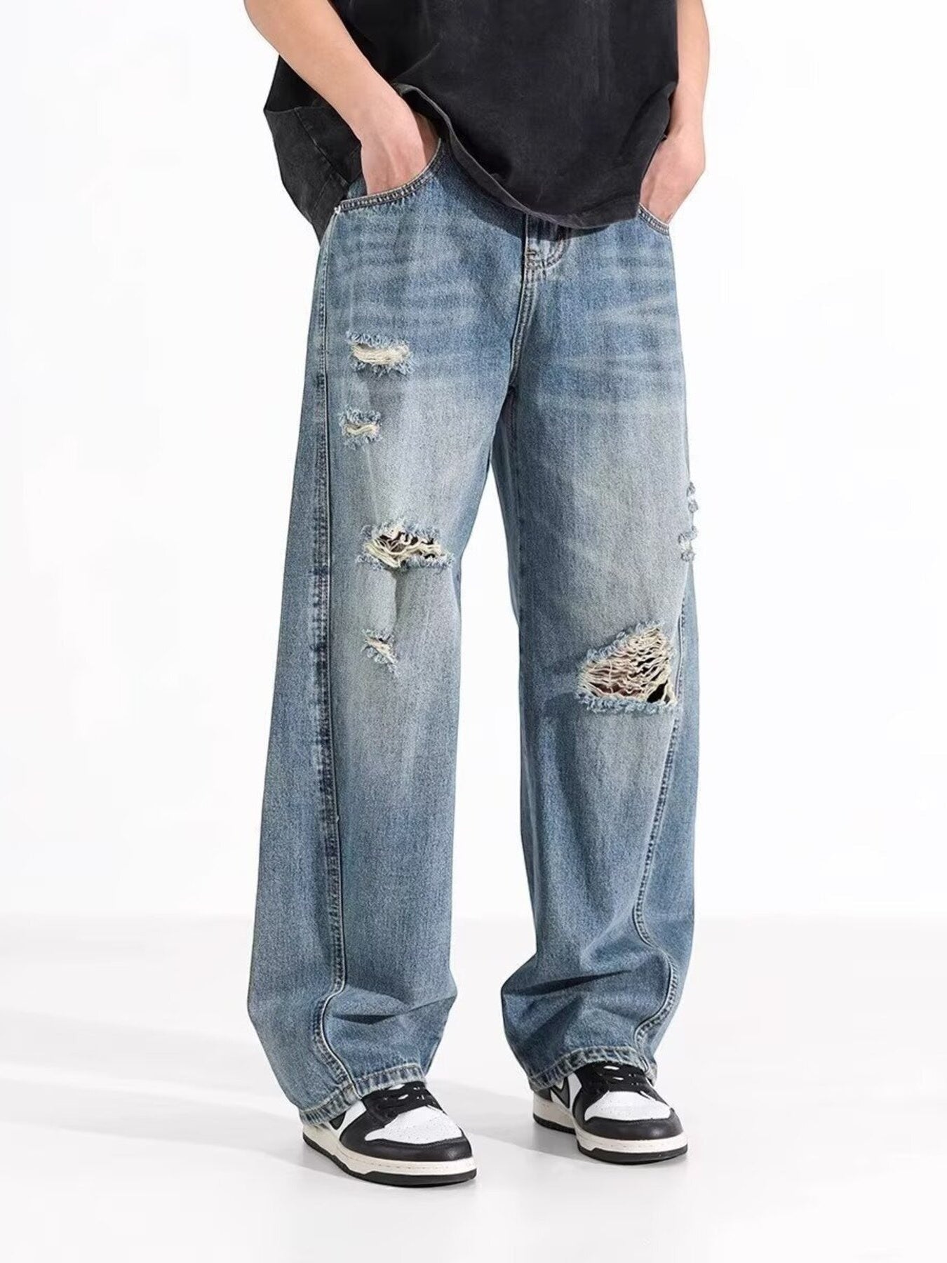 Omina blue wash distressed wide leg denim jeans with a relaxed fit, worn by a person with hands in pockets.