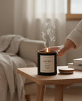 Omina Essence black candle with a wooden lid, featuring a cream label with "WITHIN" and scent notes of white tea, bergamot, and cashmere.