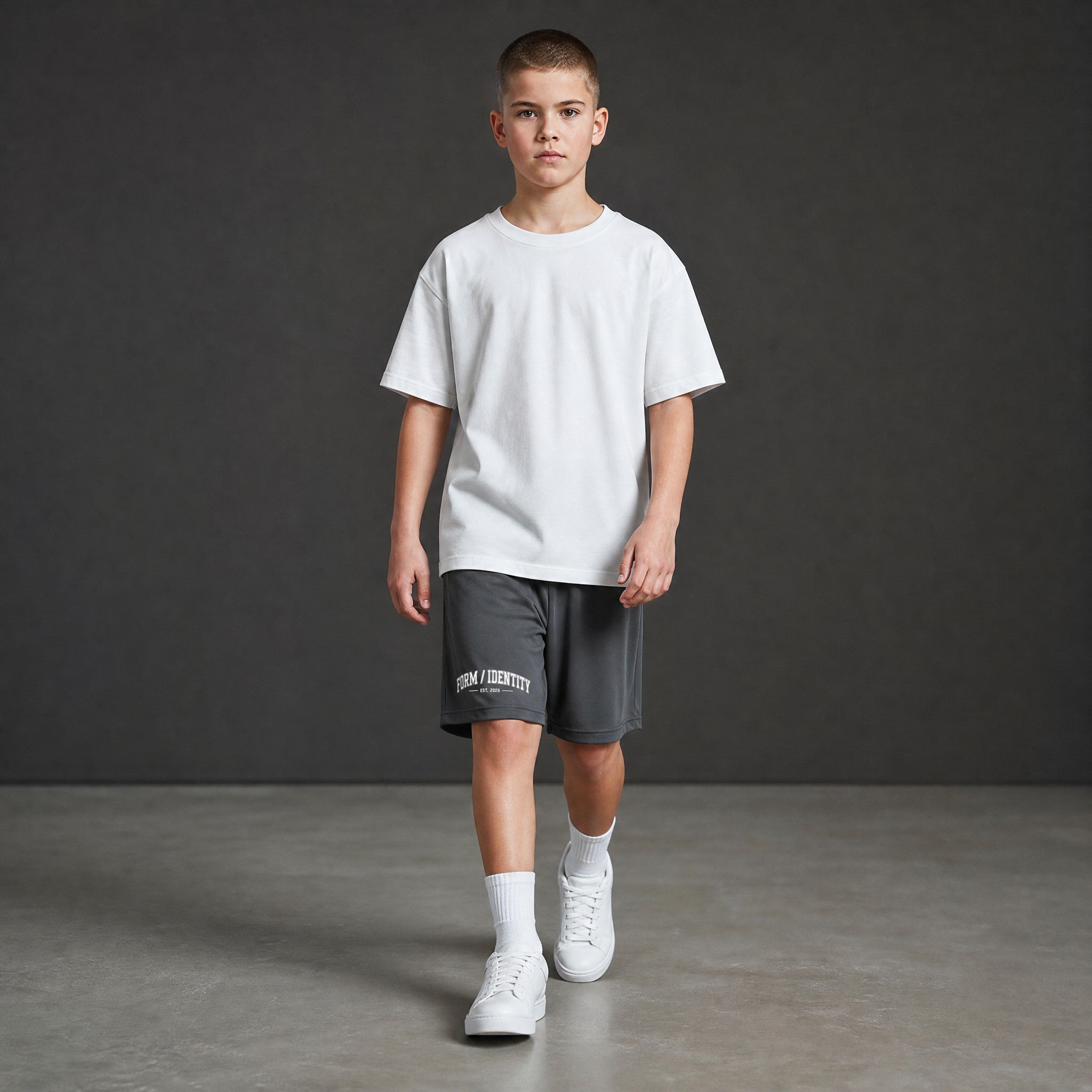 Omina Kids Youth Form / Identity shorts in dark grey with an elastic waistband and white text graphic on the left leg.
