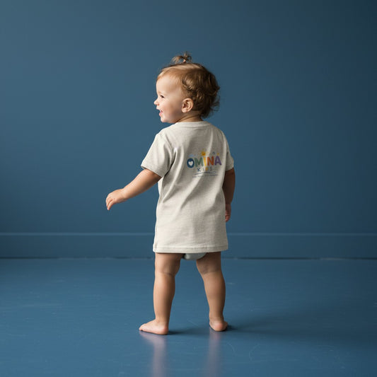 Omina Kids infant tee in heather beige, 100% combed cotton, with a playful rainbow logo on the back.