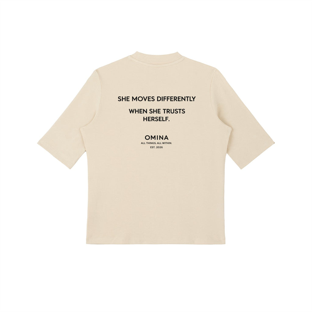 Omina cream mock neck short sleeve t-shirt with "SHE MOVES DIFFERENTLY WHEN SHE TRUSTS HERSELF." graphic.