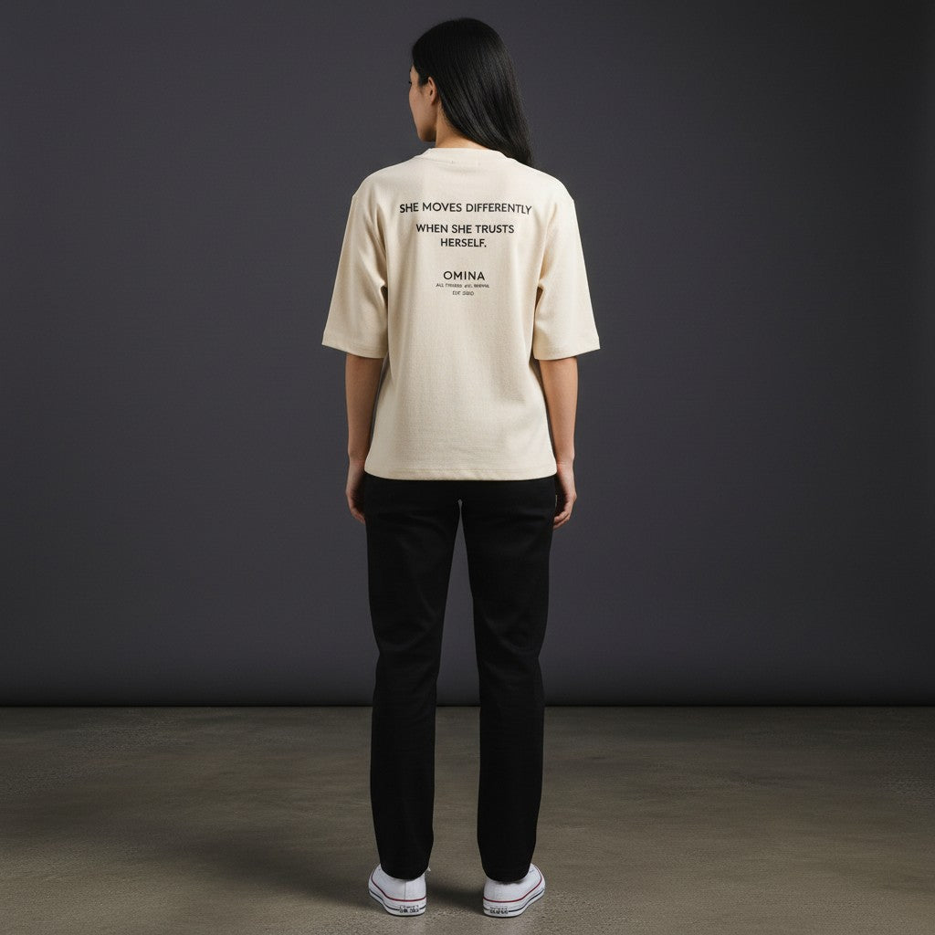 Omina cream mock neck short sleeve t-shirt with "SHE MOVES DIFFERENTLY WHEN SHE TRUSTS HERSELF." graphic and brand logo.