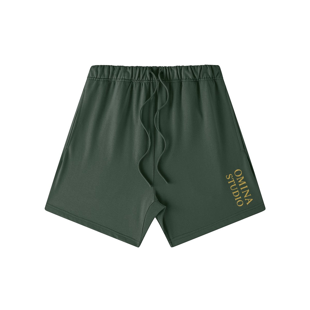 Omina Studio heavyweight dark green cotton French terry shorts with drawstring and gold logo.
