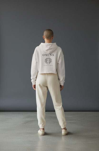 Omina Studio cream lightweight cropped hoodie with adjustable drawstring hood and raw hem. Features Omina Studio logo and graphic.