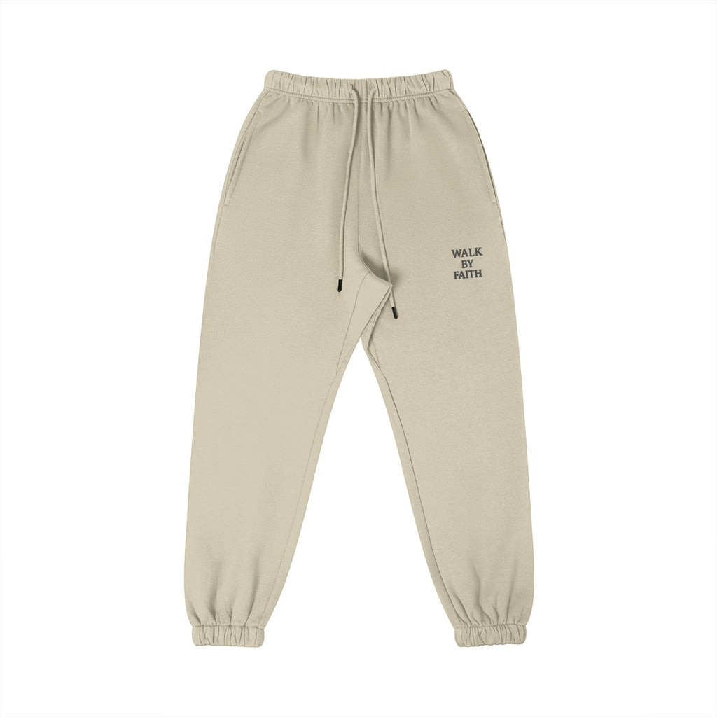 Omina Studio beige cotton sweatpants with "WALK BY FAITH" embroidered on the left thigh. Features an elastic waistband, drawstring, and tapered leg.