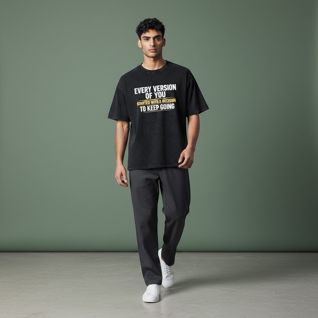 Omina black vintage wash 100% cotton unisex t-shirt with a loose fit, drop shoulders, and round neck. Features white text that reads "EVERY VERSION OF YOU STARTED WITH A DECISION TO KEEP GOING".