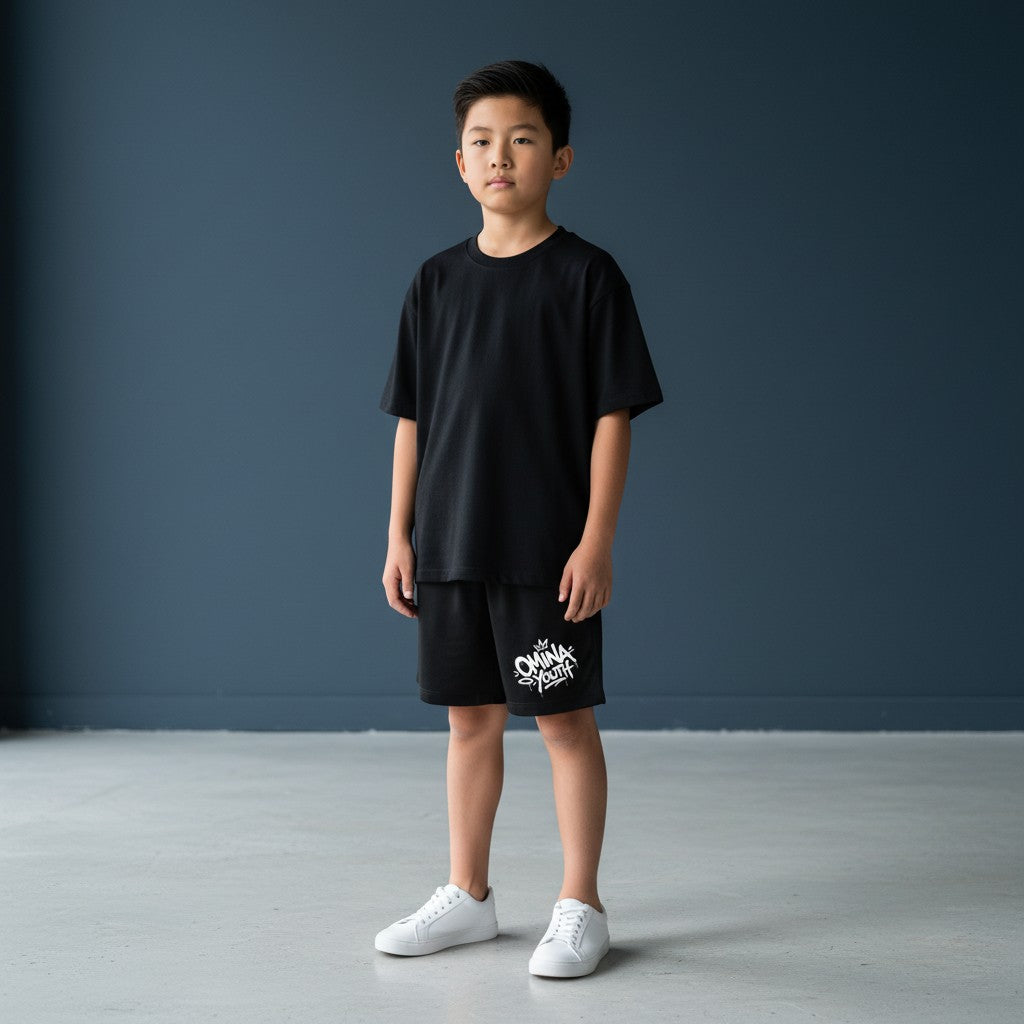 Omina Youth black relaxed fit shorts with white graffiti-style logo on the left leg. Elastic waistband.