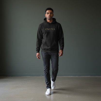 Omina Studio black essential hoodie with kangaroo pocket and gold logo on a man walking.